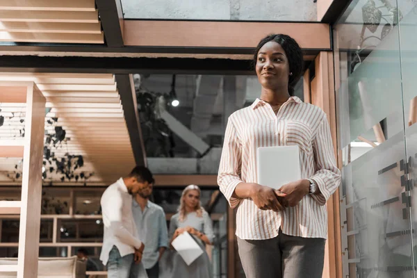 陽気なアフリカ系アメリカ人の実業家がデジタルタブレットを見て持ち 多文化の同僚が背景に立って — ストック写真