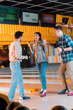 Heyecanlı Afrikalı Amerikalı kız, bowling kulübündeki mutlu, çok kültürlü arkadaşlarının jestlerini gösteriyor.