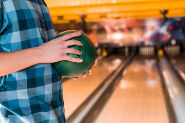 cropped view of young man holding bowling ball near skittle alley clipart