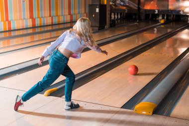 Genç sarışın kadın Skittle sokağına bowling topu atıyor.
