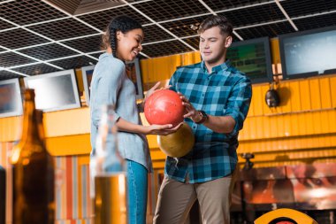 Yakışıklı bir adamın, gülümseyen Afrikalı Amerikalı bir kıza bowling topu göstermesi. 