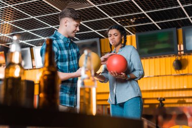 Seçici odak noktası, gülen adamın elinde bowling topları tutarken canı sıkkın Afrikalı Amerikalı bir kızla konuşması.