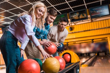 Neşeli arkadaşlar bowling kulübünde bowling toplarını seçiyor.