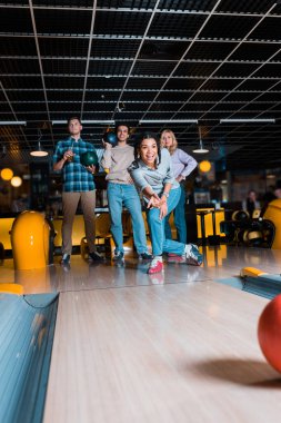 Heyecanlı Afrikalı Amerikalı kız, çok kültürlü arkadaşlarının yanındaki Skittle sokağına bowling topu atıyor.