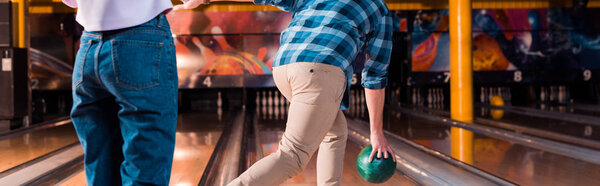 cropped view of girl standing near man throwing bowling ball on skittle alley, panoramic shot