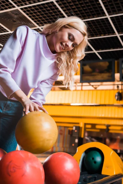 Neşeli sarışın kız bowling kulübünde bowling topu alıyor.
