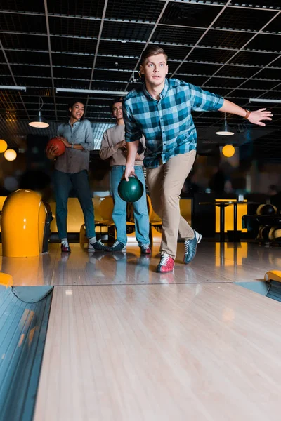 Koncentrált Fiatalember Dobott Bowling Tál Skittle Sikátorban Közelében Multikulturális Barátok — Stock Fotó