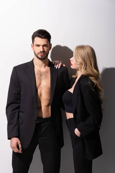 attractive young woman looking at muscular man in formal wear on white