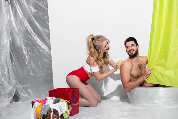happy pin up woman washing handsome man with sponge on white