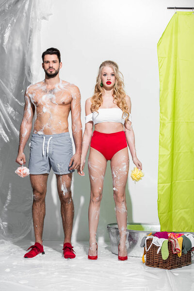 sexy pin up girl holding wet sponge with soap near shirtless man on white 