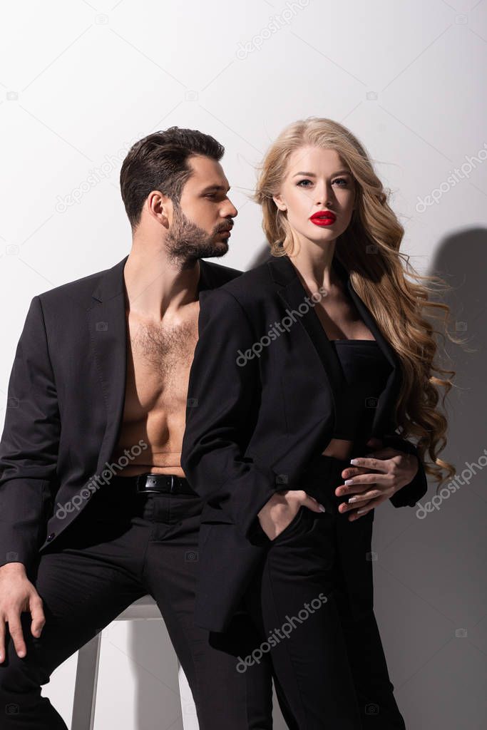 bearded man sitting on chair and looking at beautiful woman on white 