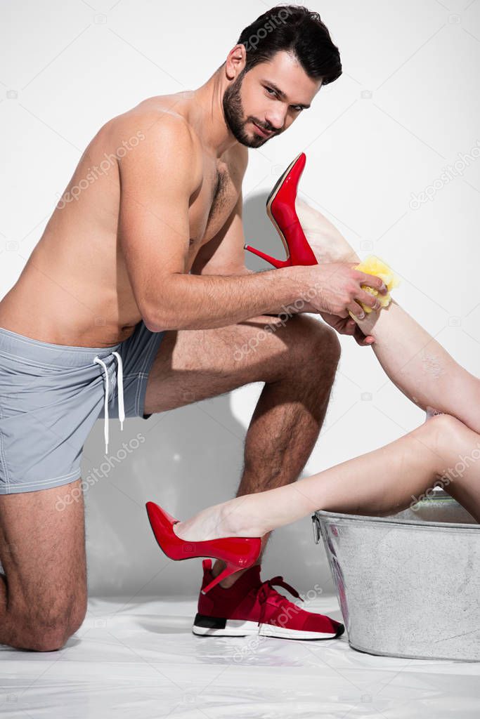 muscular man washing leg of pin up woman with sponge on white 