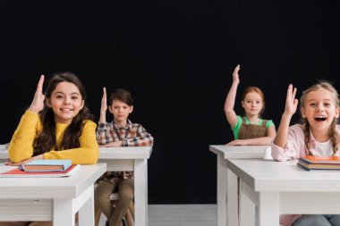 selective focus of happy schoolkids with raised hands isolated on black clipart