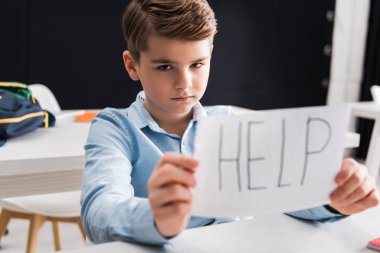 selective focus of depressed schoolkid holding paper with help lettering, bullying concept clipart