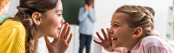 panoramic shot of schoolgirls gossiping near upset classmate, bullying concept 