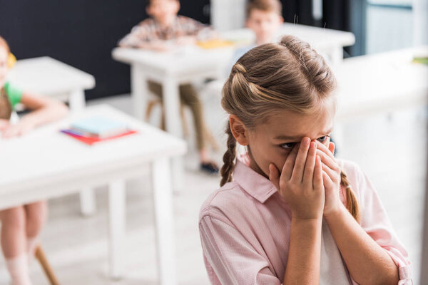 selective focus of upset schoolkid crying near classmates, bullying concept 