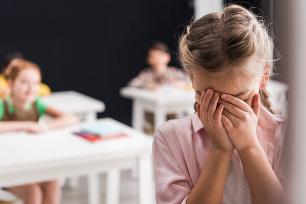 selective focus of frustrated schoolkid crying near classmates, bullying concept 
