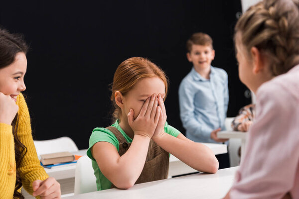 selective focus of upset kid crying near classmates on black, bullying concept 