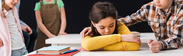 panoramic shot of schoolboy touching upset schoolgirl near classmates isolated on black, bullying concept 