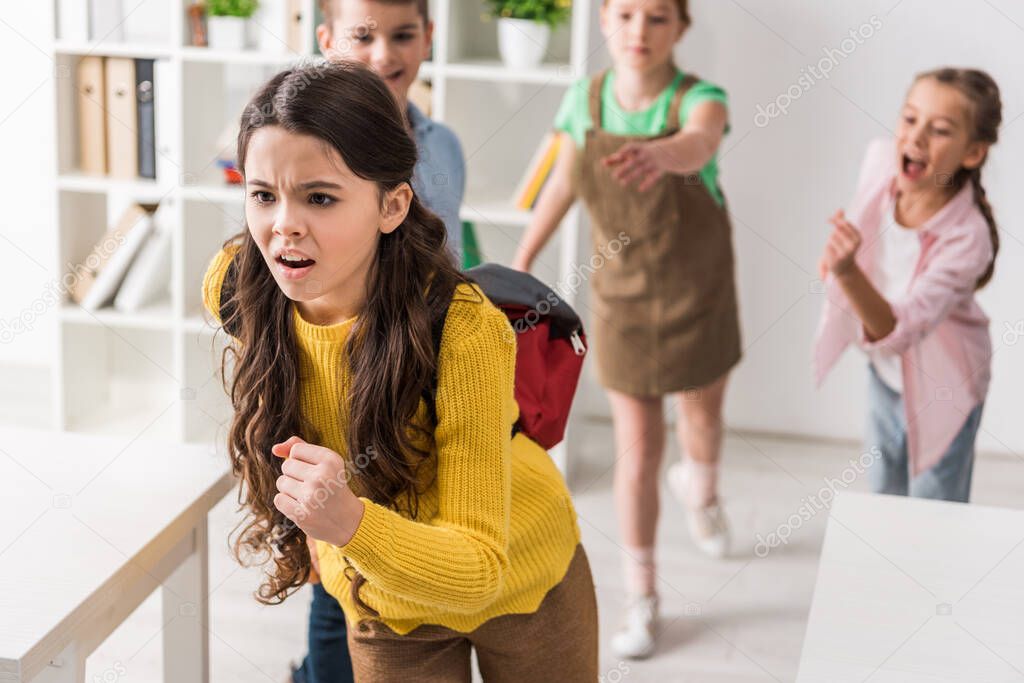 selective focus of bullied schoolgirl running from cruel classmates, bullying concept