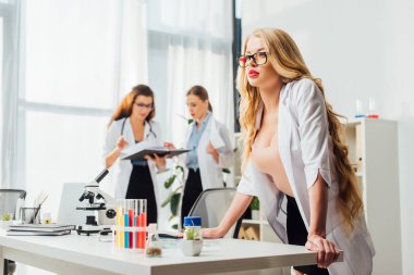 Laboratuvarda kadınların yanında gözlüklü ve beyaz önlüklü seksi hemşirenin seçici odağı 