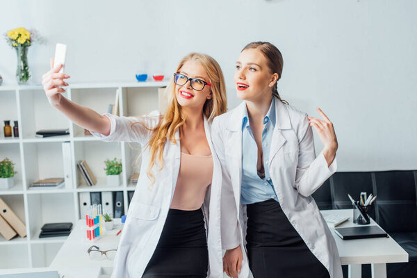 счастливые и сексуальные медсестры в белых халатах делают селфи в больнице
 