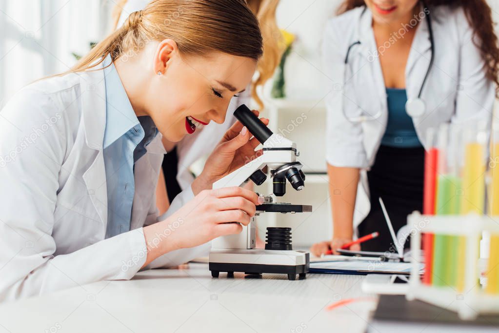 selective focus of happy girl looking through microscope near sexy nurses 