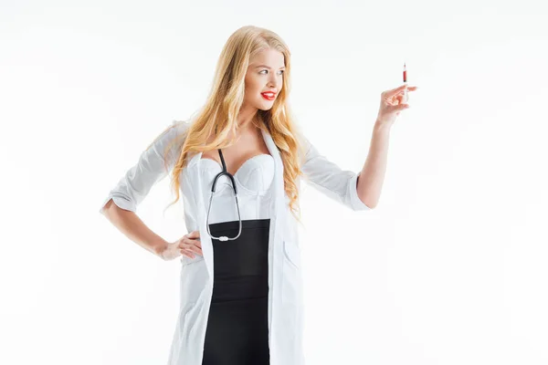 一位快乐而性感的护士一边站在那里一边看着注射器 一边手放在胸前 与白色隔离 — 图库照片