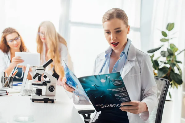 女性身边的性感护士阅读科学杂志和显微镜的选择焦点 — 图库照片