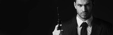Monochrome image of gangster holding gun and looking at camera isolated on black, panoramic  shot clipart