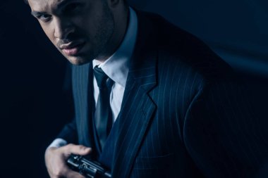 Silahlı bir gangster karanlık arka planda şüpheli bir şekilde kameraya bakıyor.