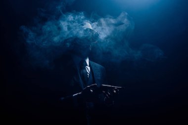 Gangster silueti silah tutuyor ve karanlık arka planda sigara içiyor.