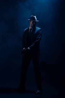 Dangerous gangster holding weapon on dark blue background clipart