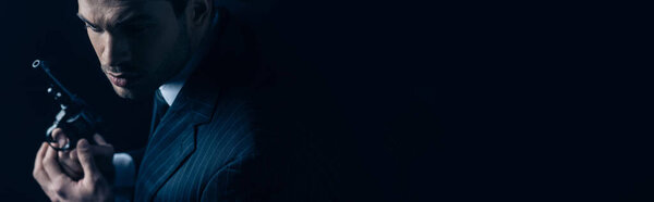 Гангстер держит револьвер на темном фоне, панорамный снимок
