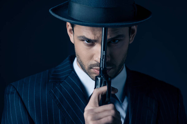 Portrait of gangster holding gun in front of face on dark blue