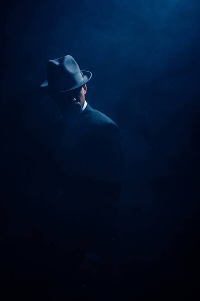 Silhouette of mafioso in suit and felt hat on dark blue background