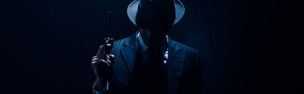 Силуэт гангстера, поднимающего пистолет на темно-синем фоне, панорамный снимок
