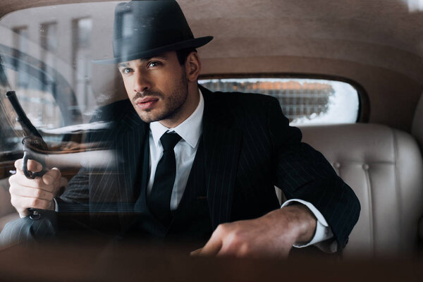 Selective focus of confident mafioso holding gun in car