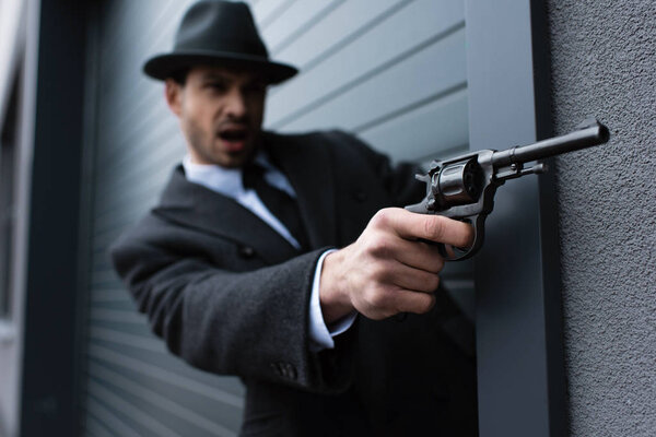 Selective focus of mafioso aiming gun with outstretched hand near wall on street
