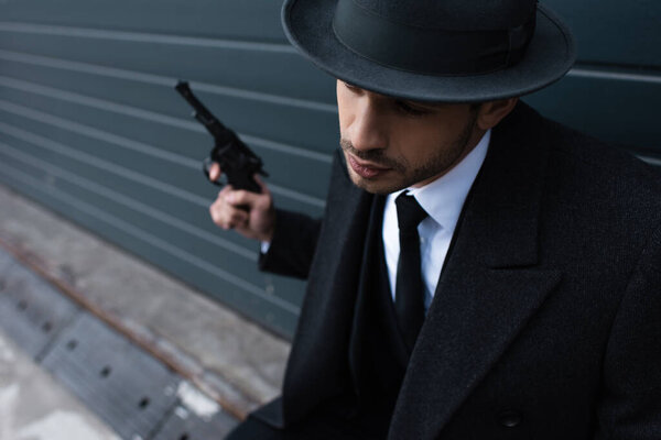 Selective focus of gangster holding revolver near wall on street