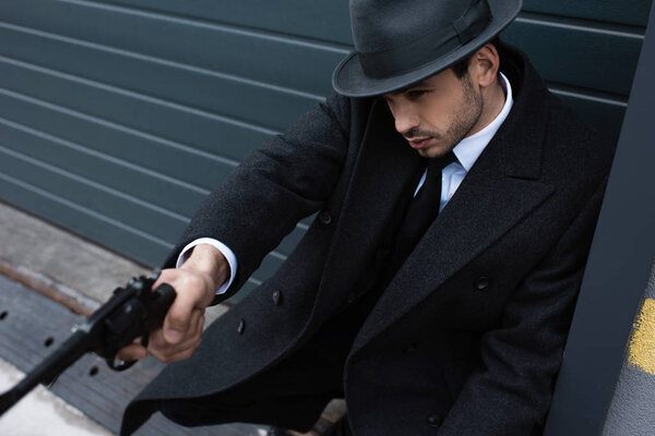 Selective focus of mafioso with outstretched hand aiming weapon near wall on street