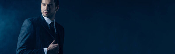 Уверенный мафиози смотрит в сторону на темном фоне, панорамный снимок
