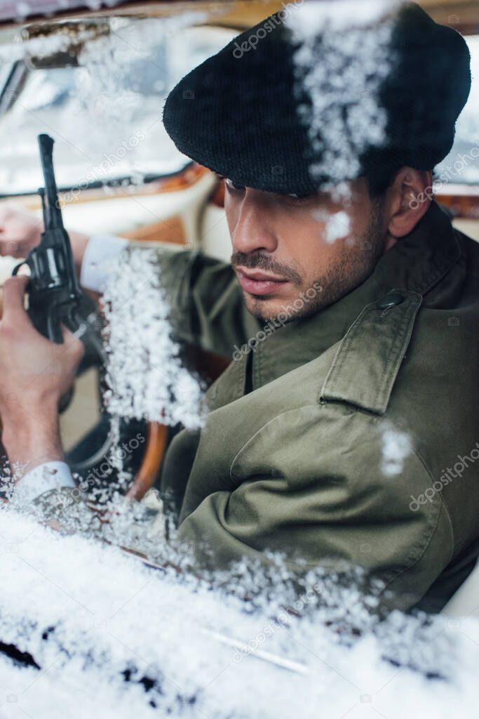 Selective focus of mafioso with gun in car covered with snow