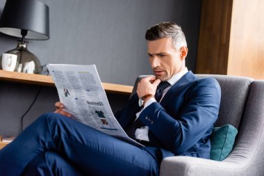 Takım elbiseli iş adamı koltuğunda oturuyor ve otelde gazete okuyor. 