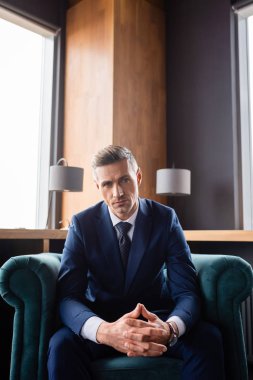 Takım elbiseli işadamı, elleri sımsıkı bağlı koltukta oturuyor ve kameraya bakıyor.