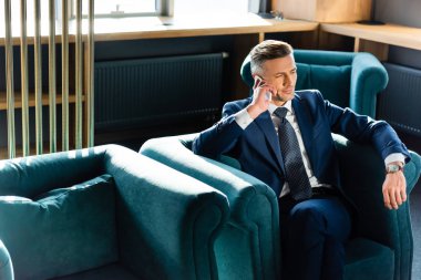 Takım elbiseli iş adamı akıllı telefonla konuşuyor ve koltukta oturuyor. 