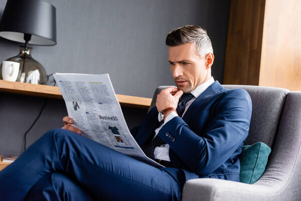 businessman in suit sitting in armchair and reading newspaper in hotel 