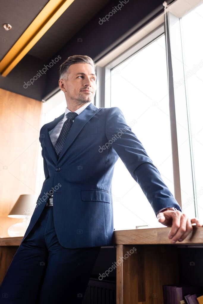 low angle view of smiling businessman in suit looking through window 