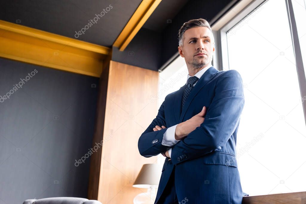 low angle view of businessman in suit with crossed arms looking away 