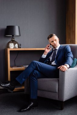 Takım elbiseli iş adamı akıllı telefonla konuşuyor ve koltukta oturuyor. 